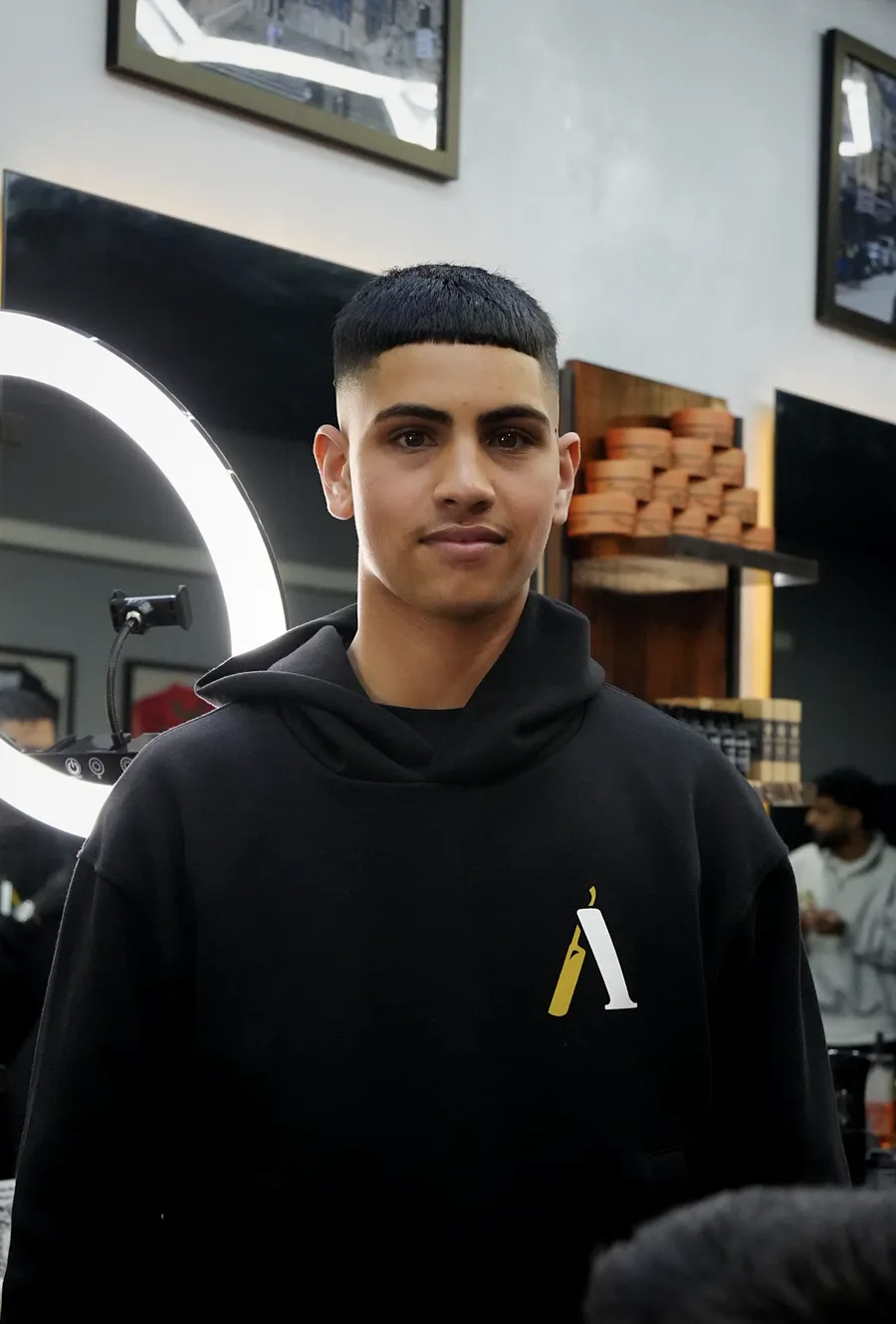 Abz, barber at Atta Barbershop, in the shop's black hoodie